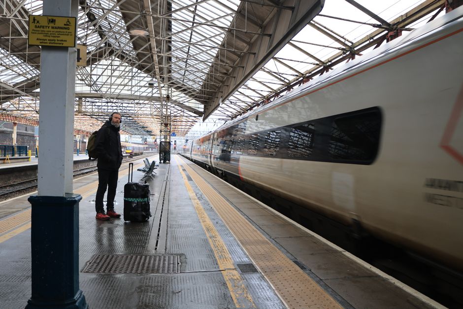 A traveler with a small carry-on suitcase and backpack standing on a European train platform, ready for their journey.